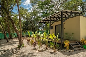 A small, single-story structure with a covered patio area, surrounded by trees and plants.