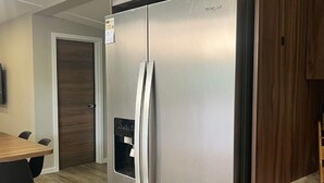 Un refrigerador d'acer inoxidable amb dispensador d'aigua, una taula de dinar de fusta amb cadires i un armari de fusta.