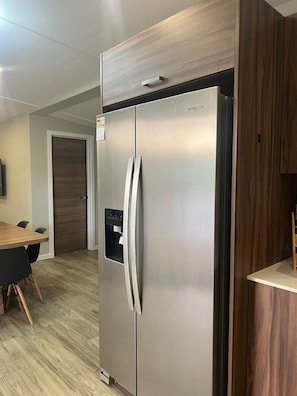 A stainless steel refrigerator with a water dispenser, a wooden dining table with chairs, and a wooden cabinet. - CASA PANDO: Tamarindo 2 homes Garden Retreat (tamarindo)