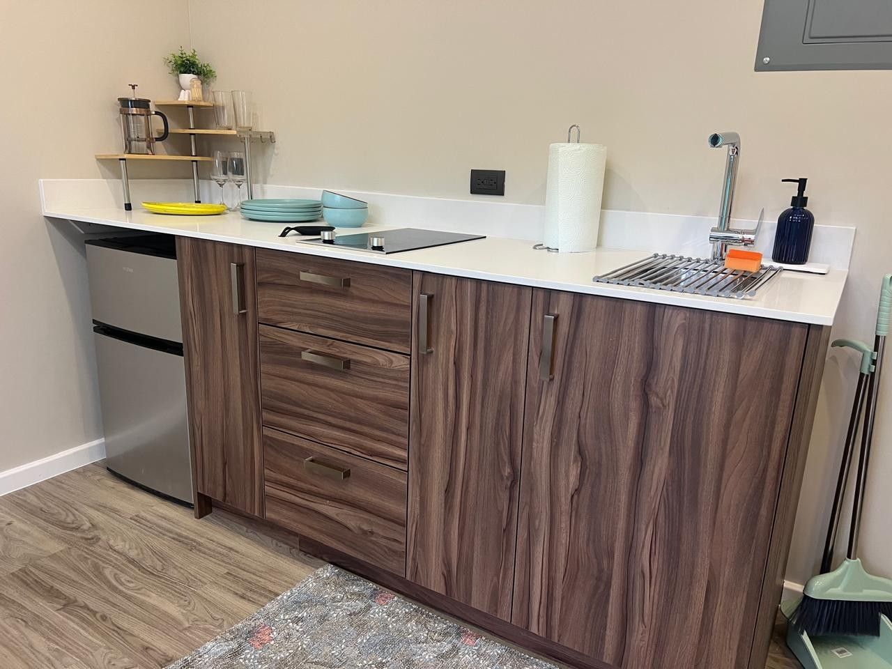 A kitchen with wooden cabinets, a white countertop, a stainless steel refrigerator, and a sink with a faucet.