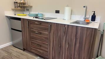 A kitchen with wooden cabinets, a white countertop, a stainless steel refrigerator, and a sink with a faucet.