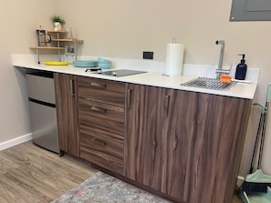 A kitchen with wooden cabinets, a white countertop, a stainless steel refrigerator, and a sink with a faucet.