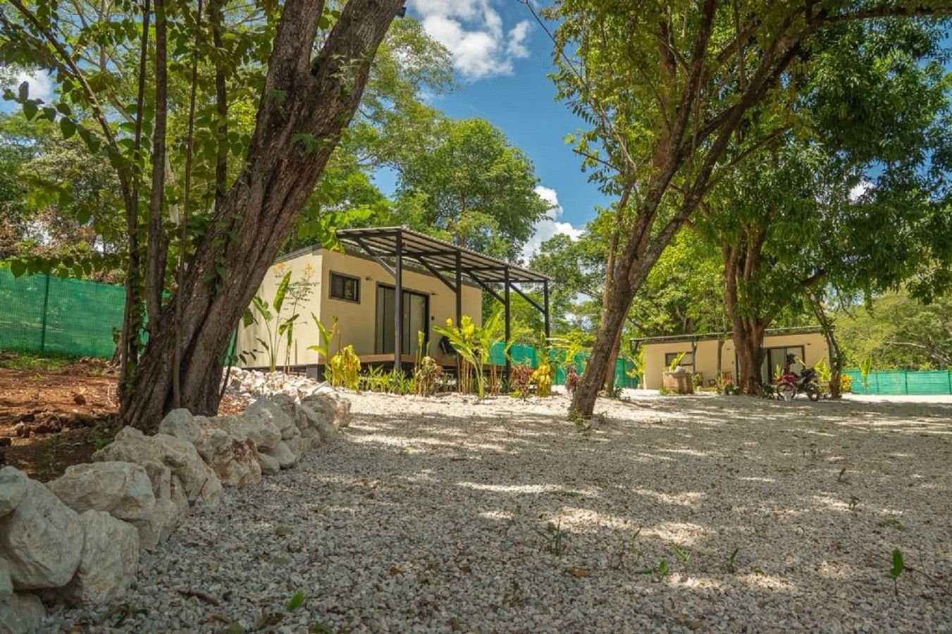 A building with a covered patio area, surrounded by trees and gravel.