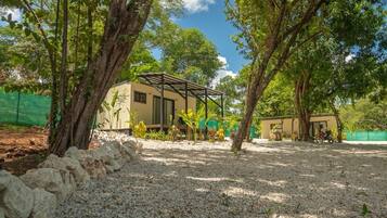 A building with a covered patio area, surrounded by trees and gravel.