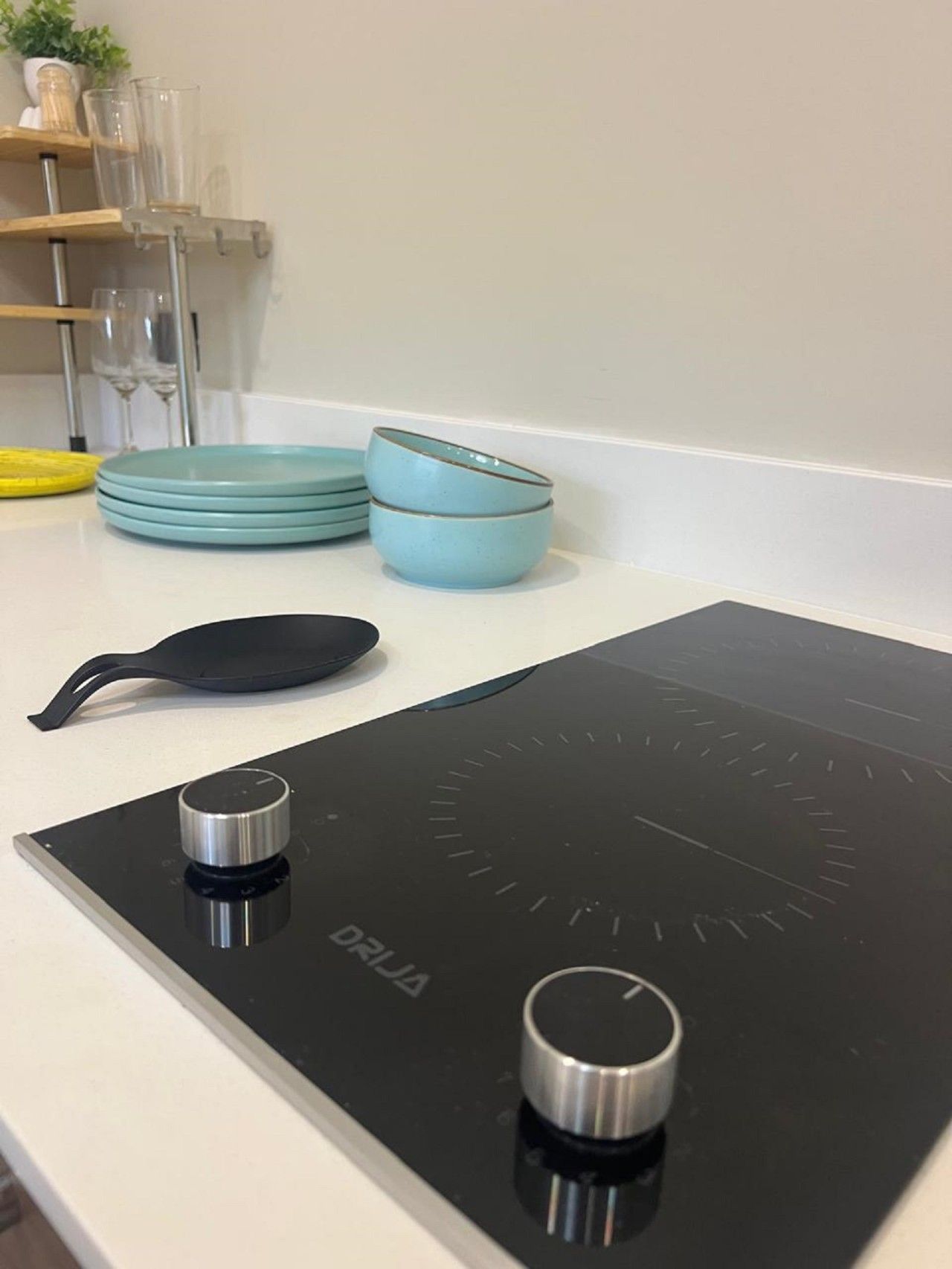 A kitchen counter with a black induction cooktop, a black pan, and a stack of blue plates.