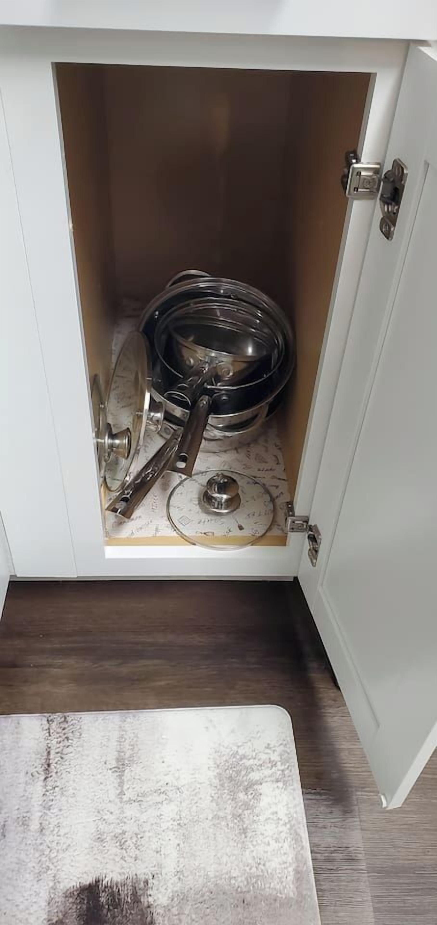 A cabinet with a door open, revealing kitchen utensils and a pot inside.