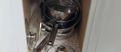 A cabinet with a door open, revealing kitchen utensils and a pot inside.
