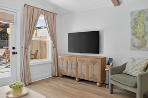 Een woonkamer met een televisie, een bank, een kast en een raam met gordijnen.
