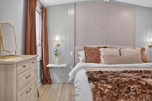 Een slaapkamer met een bed, een kaptafel, een spiegel, een wandlamp en een behang met een patroon.