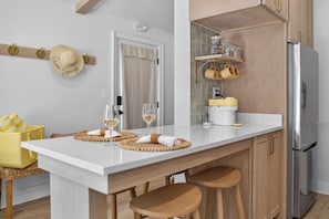 Een moderne keuken met een wit aanrecht, houten krukken, een roestvrijstalen koelkast en een opbergmand.