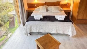 Un dormitorio con techo de madera, una cama con ropa de cama blanca, dos lámparas de noche y una pequeña mesa de madera.