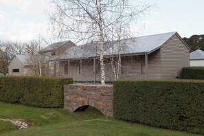 Ein Haus mit einer Steinbrücke, einer Holzveranda und einer gepflegten Hecke.