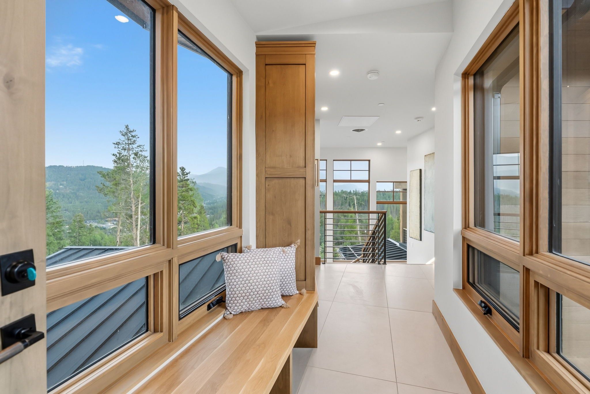 A modern interior with large windows, a wooden bench, and a staircase leading to a balcony.