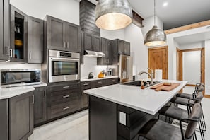 A modern kitchen with dark cabinetry, stainless steel appliances, and a central island with bar stools. - Vista - The Best View in Breckenridge (Breckenridge)