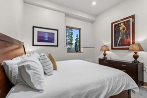 A hotel room with a large bed, a dresser, two lamps, a framed picture, and a window with a view of trees. - Vista - The Best View in Breckenridge (Breckenridge)