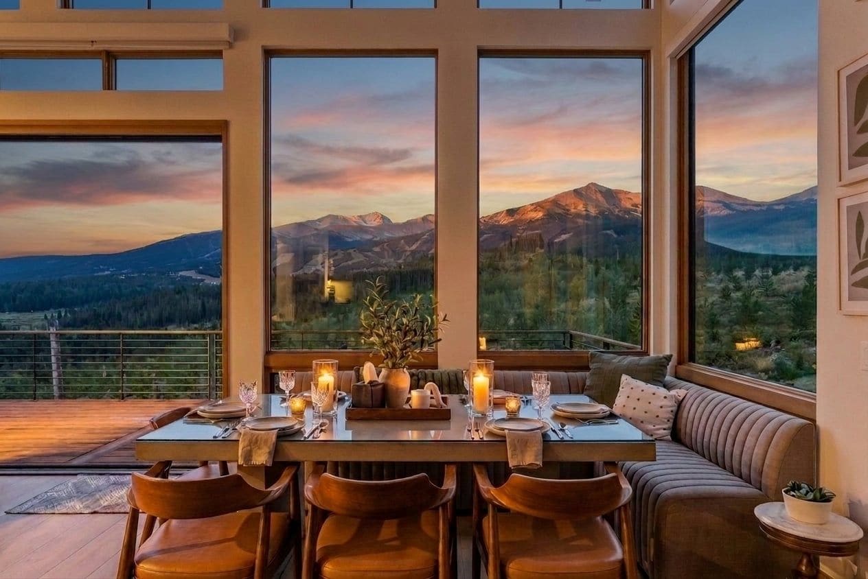 A dining area with a table set for four, large windows with a mountain view, and a cozy seating arrangement.