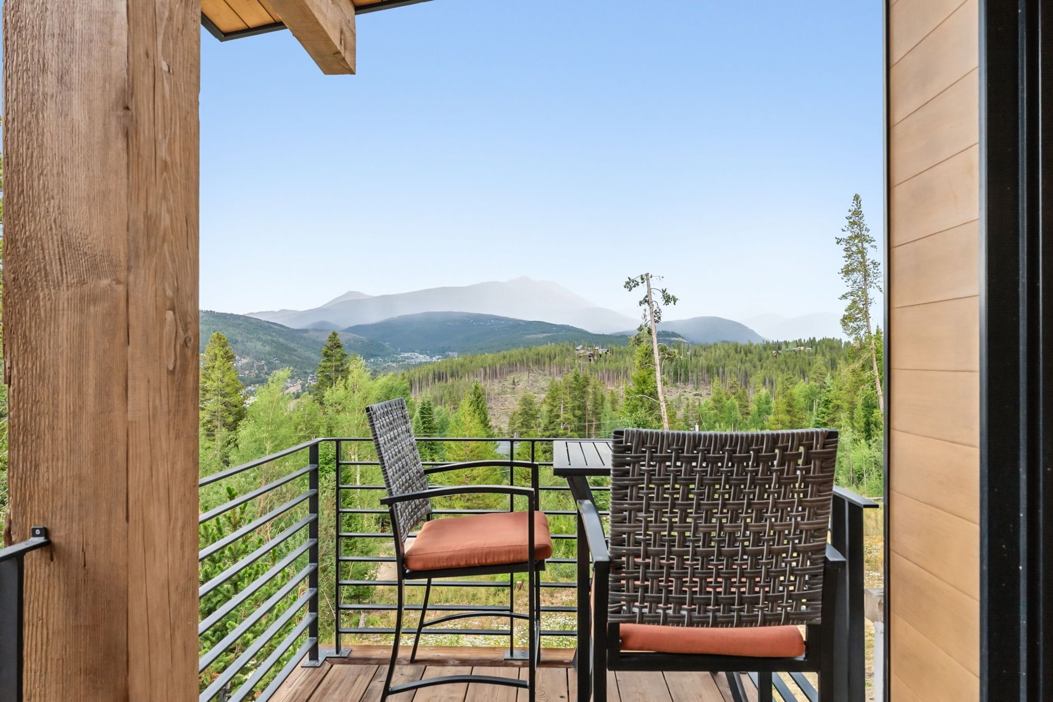Un balcon avec deux chaises et une table, donnant sur une chaîne de montagnes boisée.