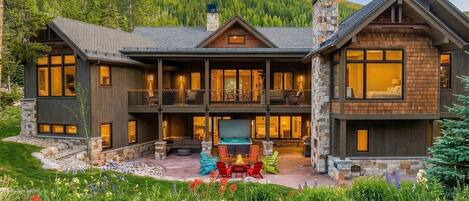 A large, two-story lodge with a stone facade, multiple windows, and a patio area with outdoor seating.