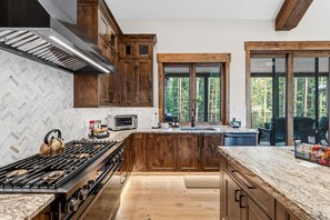 Eine moderne Küche mit Holzausstattung, einem Gasherd, einer Mikrowelle und einem großen Fenster mit Blick auf einen Wald.