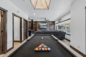 A pool table with a pool cue and balls, a ceiling fan, and a view of the outdoors. - 🏔️ Leika Haus | Riverfront Luxury ♨️ Hot Tub + Barrel Sauna 🎬 Theater Lounge | Sleeps 19 (Keystone)