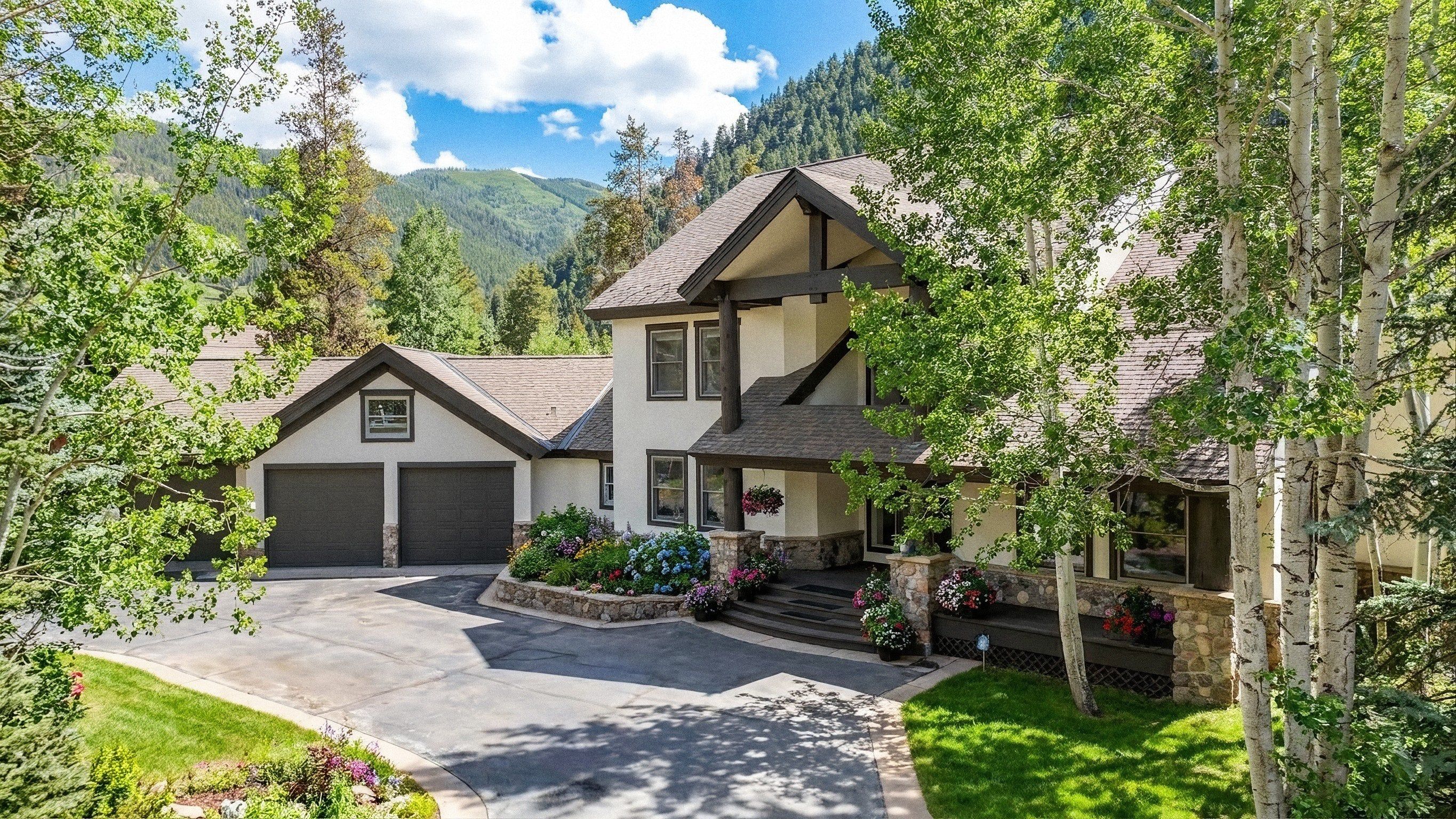 A two-story house with a garage, surrounded by lush greenery and mountains.
