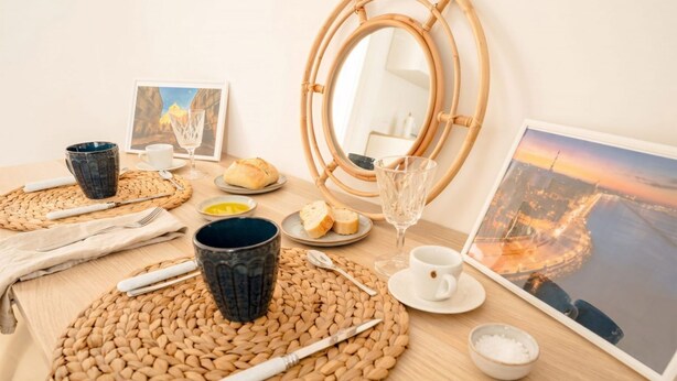 A breakfast setup with a woven placemat, a black mug, a white cup, a glass, a plate with bread, and a small bowl of sugar. - ALL Vecchia Bari | Historic Charm in the Heart of Old Town (Bari)