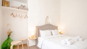 A bedroom with a bed, bedside tables, a chair, a shelf with towels, and a vase with flowers. - ALL Vecchia Bari | Historic Charm in the Heart of Old Town (Bari)