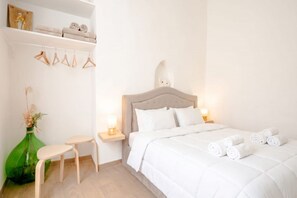 A bedroom with a bed, bedside tables, a chair, a shelf with towels, and a vase with flowers. - ALL Vecchia Bari | Historic Charm in the Heart of Old Town (Bari)