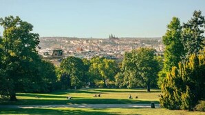 A park with open grassy areas, trees, and a distant view of a cityscape with buildings and a tower. - Modern City Apartment (Prague 2)