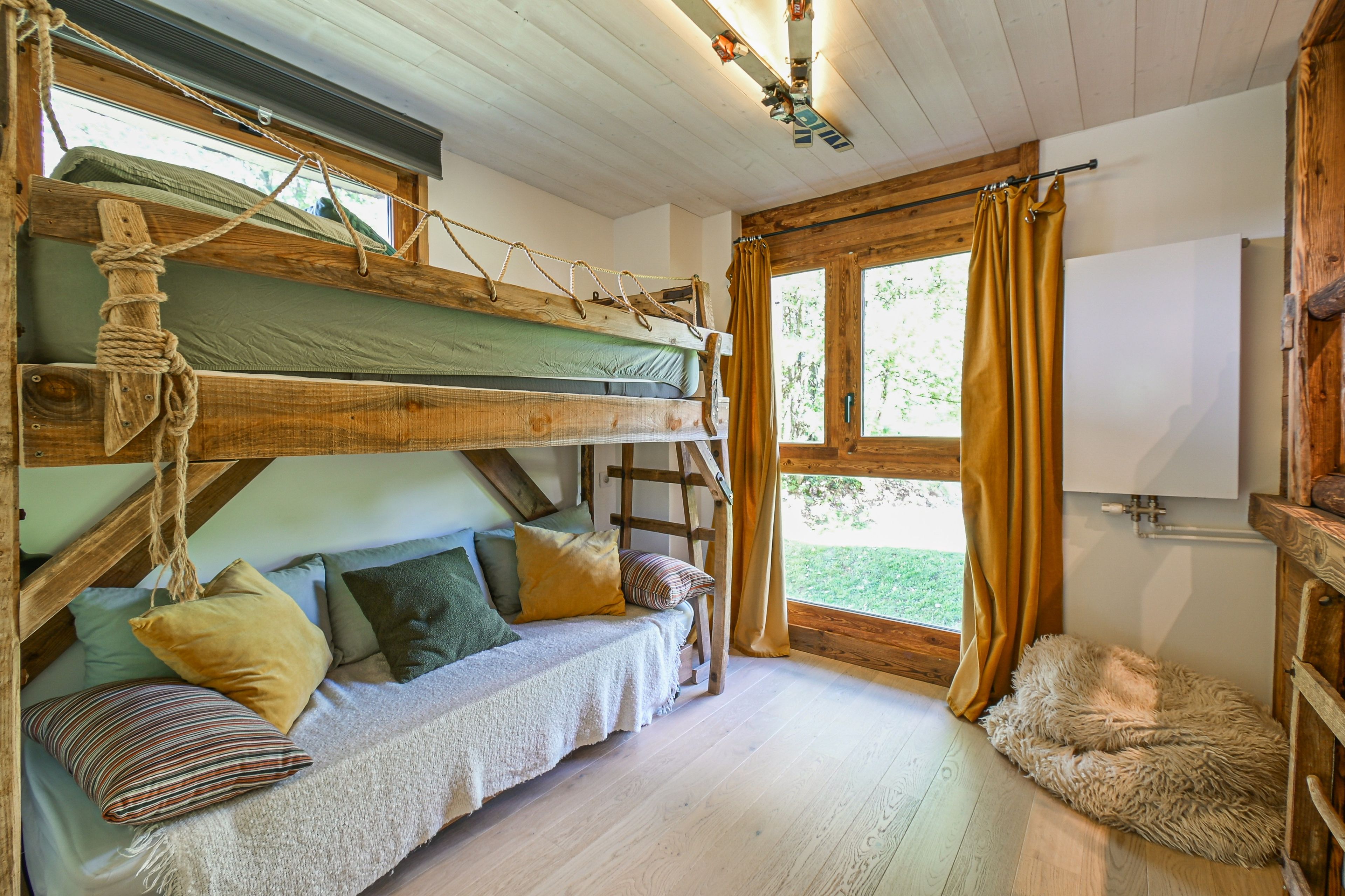Une pièce confortable avec un lit superposé, un petit canapé avec des coussins, un tapis moelleux et une fenêtre avec des rideaux.