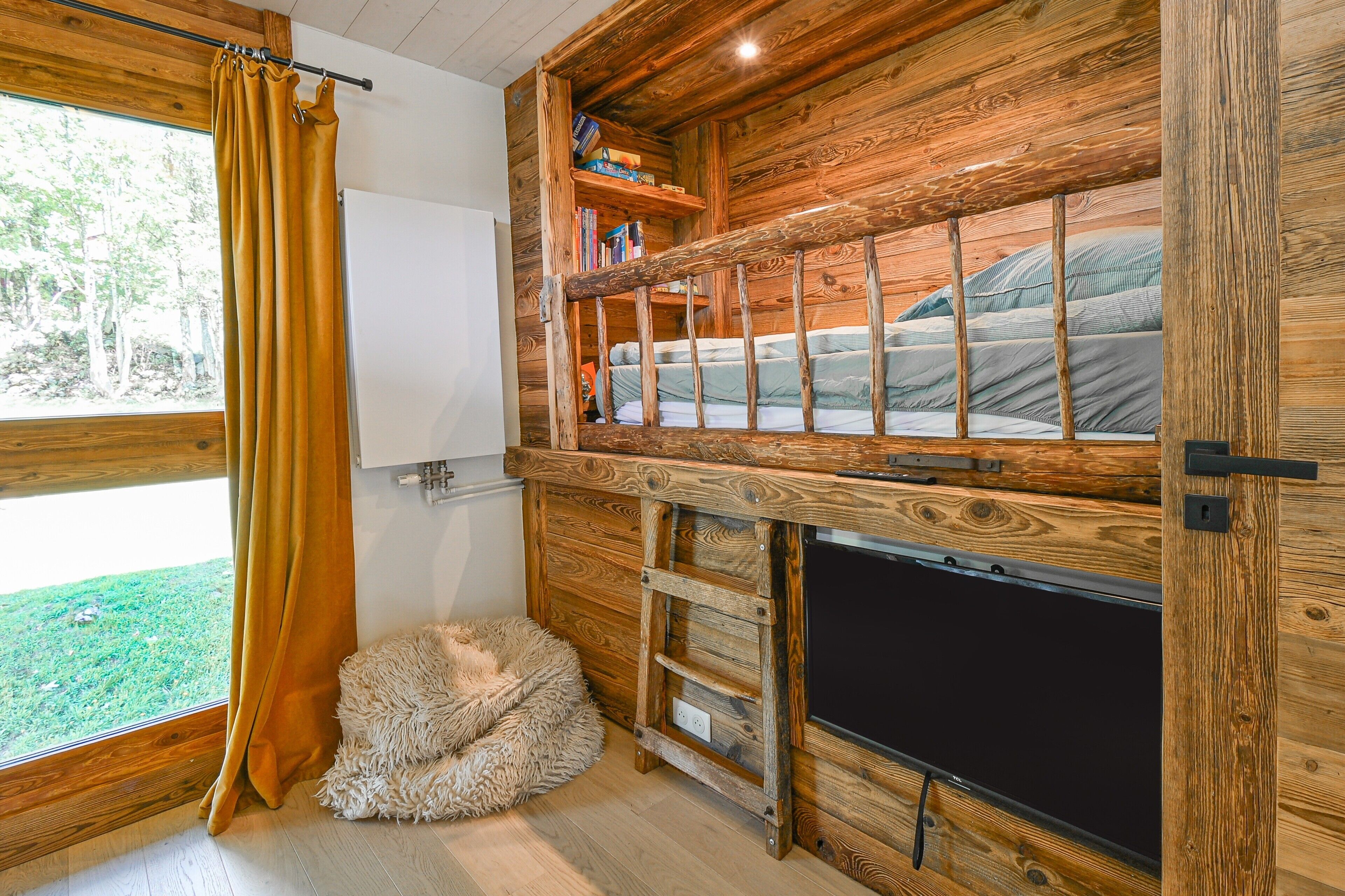 Uma cabana com beliche, um pequeno sofá, uma janela com cortinas e uma parede de madeira.