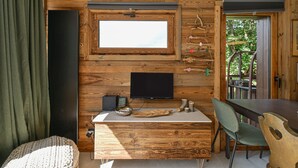 A wooden interior with a television mounted on the wall, a dining table, and a chair.