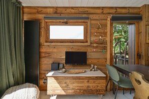 A wooden interior with a television mounted on the wall, a dining table, and a chair.