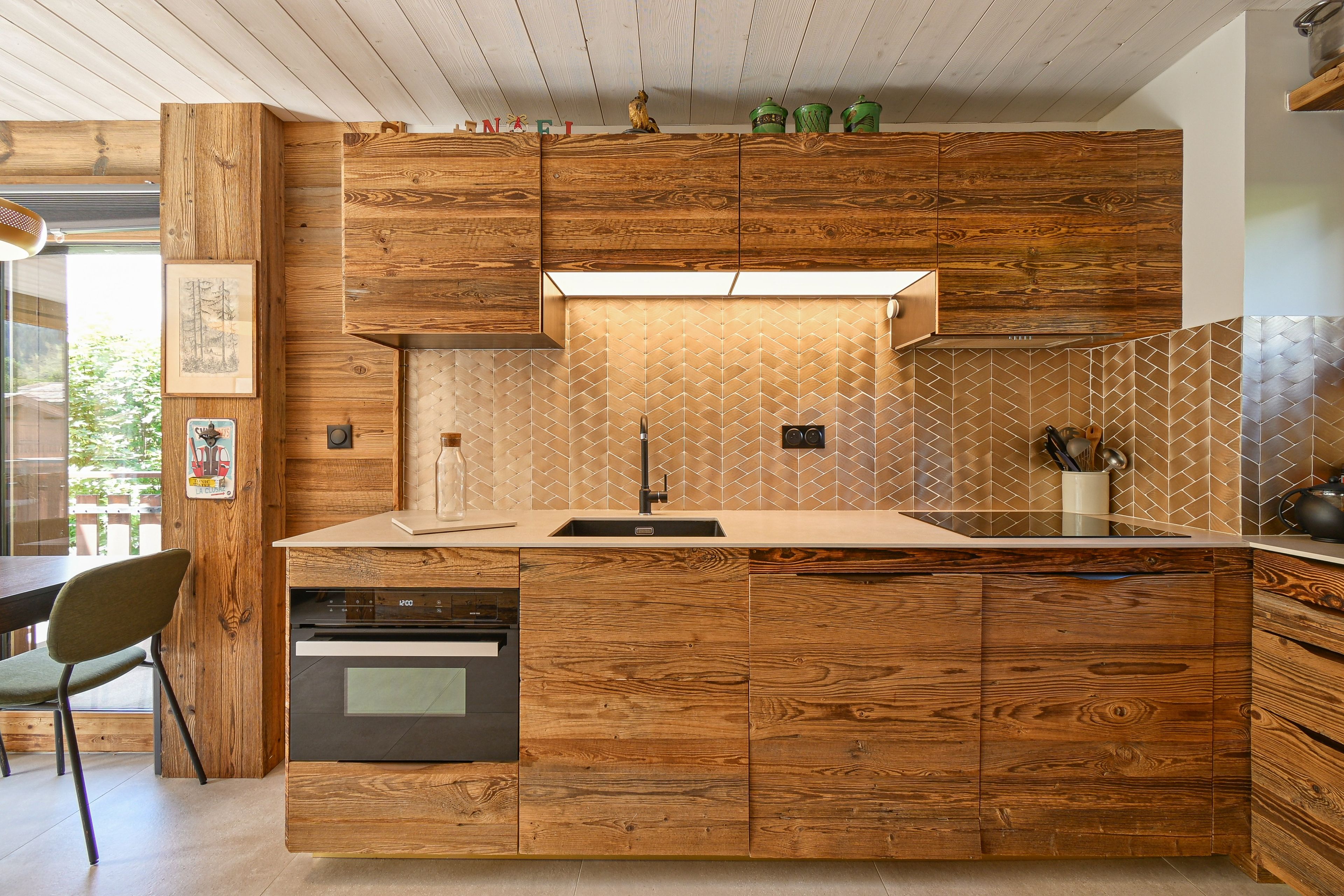 Cozinha moderna com armários de madeira, forno embutido e painel de azulejos em padrão herringbone.