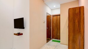 A hallway with a flat-screen TV mounted on the wall, a wooden door, and a green mat at the entrance. - Deluxe The Royal Orbit (Barasat)