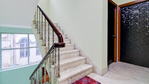A staircase with marble steps and a wooden handrail, leading to a door with a number plate. - Deluxe The Royal Orbit (Barasat)