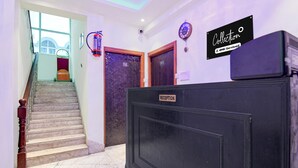 A hotel reception area with a reception desk, a clock, and a staircase leading to a room. - Deluxe The Royal Orbit (Barasat)