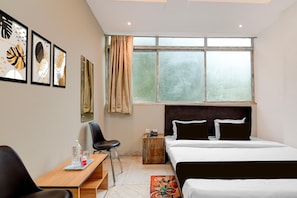 Ein Hotelzimmer mit Bett, Schreibtisch mit Stuhl, Fenster mit Vorhängen und einem Bild an der Wand.