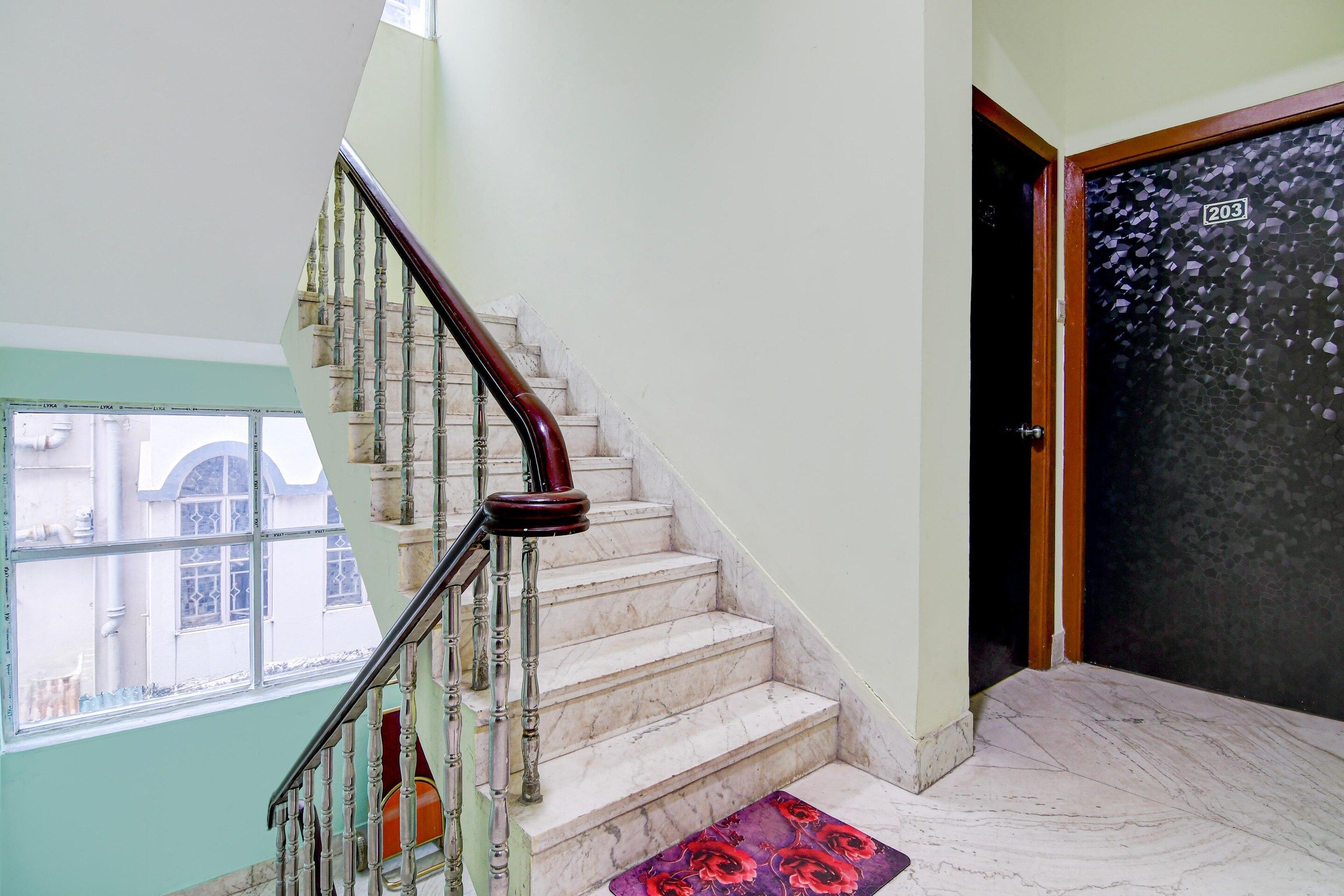 A staircase with marble steps and a wooden handrail, leading to a door with a number plate.