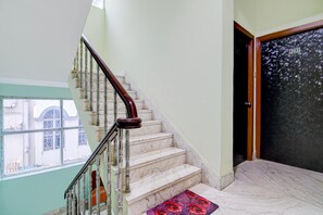 A staircase with marble steps and a wooden handrail, leading to a door with a number plate. - Deluxe The Royal Orbit (Barasat)