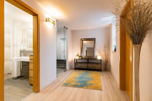 A hallway with a wooden floor, a mirror on a console table, and a vase with branches. - Garden Oasis Apartment (Prague 2)
