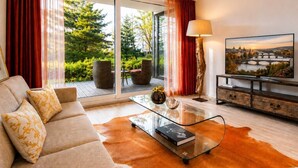 A modern living room with a sofa, a glass coffee table, a lamp, and a TV displaying a scenic view. - Garden Oasis Apartment (Prague 2)