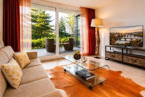 A modern living room with a sofa, a glass coffee table, a lamp, and a TV displaying a scenic view. - Garden Oasis Apartment (Prague 2)