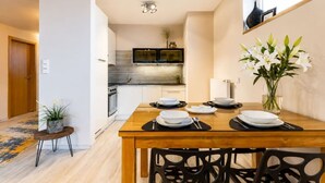 A dining area with a wooden table set for four, a vase of white flowers, and a view into the kitchen with a modern stove and microwave. - Garden Oasis Apartment (Prague 2)