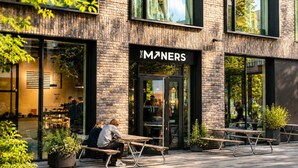 An outdoor seating area with tables and benches in front of a building with a brick facade and large windows. - Garden Oasis Apartment (Prague 2)