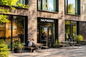 An outdoor seating area with tables and benches in front of a building with a brick facade and large windows. - Garden Oasis Apartment (Prague 2)