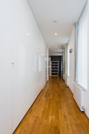 A corridor with wooden flooring, white walls, and a view into a room with a dark-colored wardrobe. - Riverside Urban Oasis • AC • Stylish Karlín (Karlín)