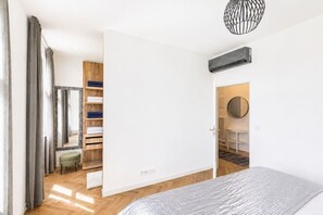 A modern bedroom with a bed, a wooden wardrobe, and a bathroom with a round mirror. - Elegant City View Apartment with AC (Praha 3-Žižkov)