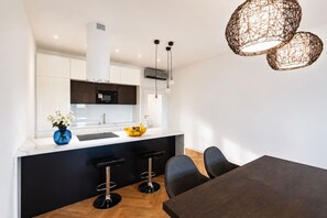 A modern kitchen with a white countertop, black bar stools, and a dining table. - Elegant City View Apartment with AC (Praha 3-Žižkov)