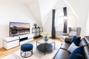 Una sala de estar moderna con televisor de pantalla plana, un sofá, una mesa de centro y una silla.